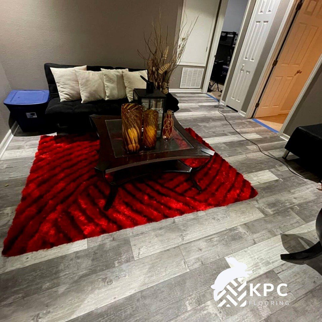 Light gray rustic wood-look plank floor in a room with a red area rug